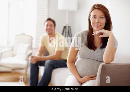 Parents en attente. Une belle femme enceinte tenant son estomac pendant que son mari est assis à l'arrière-plan. Banque D'Images