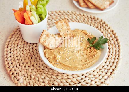 Houmous faits maison avec de l'huile d'olive, des biscuits, du persil et des légumes frais sur la table. Des collations saines végétariennes rustiques gros plan. Banque D'Images