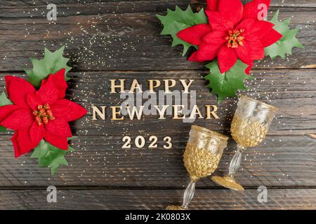 bonne année 2023 inscription en lettre de bois, fleurs de poinsettia rouges et verres à champagne sur fond de bois. Carte de vœux de fête pour le wi Banque D'Images
