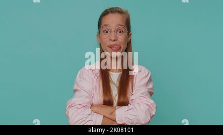 Joyeux drôle boulades adolescente fille dans la chemise. Enfant fille montrant la langue faisant des visages à la caméra, se moquer autour, plaisantant, en apantant avec le visage stupide, taquinant isolé seul sur fond bleu studio à l'intérieur Banque D'Images