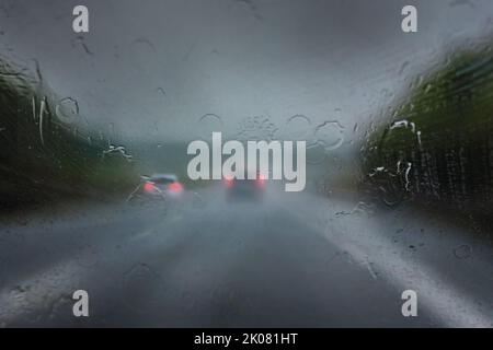 Forte pluie sur l'autoroute, grosses gouttes sur le pare-brise et voitures floues avec feux arrière rouges sur la route sombre, temps dangereux en conduisant, traff Banque D'Images