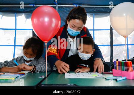 (220910) -- LUDING, le 10 septembre 2022 (Xinhua) -- Volunteer Sun Yan (C) dessine des photos avec des enfants dans une « salle de classe de tente » au refuge de secours en cake de l'école secondaire Luding no 2 à Luding, dans la province du Sichuan, dans le sud-ouest de la Chine, le 10 septembre 2022. Après un tremblement de terre de magnitude 6,8 qui a secoué le comté de Luding dans la province du Sichuan, dans le sud-ouest de la Chine, lundi, plus de 800 villageois de la ville de Detuo, dont environ 50 enfants, ont été temporairement relogés dans le lycée de Luding no 2. Depuis 6 septembre, 11 enseignants des jardins d'enfants de Luding et 10 étudiants des collèges et du secondaire se sont portés volontaires pour s'occuper de Banque D'Images