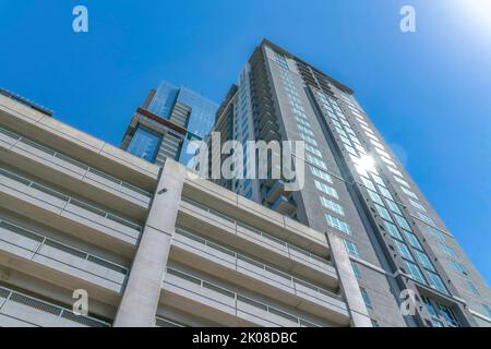 Façade de bâtiment résidentiel avec fenêtres reflétant la lumière du soleil contre le ciel bleu. Les appartements et le parking couvert donnent sur l'extérieur et disposent d'un logement moderne Banque D'Images