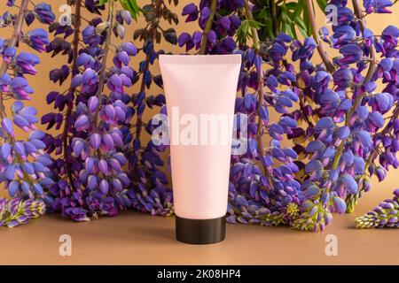 Bouteille de maquillage rose Mockup avec bouchon à vis noir et fleurs lupin bleu violet beaucoup sur fond doré brun. Crème, gel, soin de la peau Banque D'Images