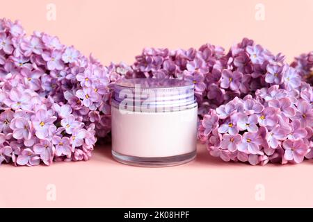 Pot blanc Mockup avec bouchon à vis métallique de crème hydratante et fleurs de lilas sur fond rose. Gros plan, soin de la peau d'été cosmétique. Marquage du produit Banque D'Images