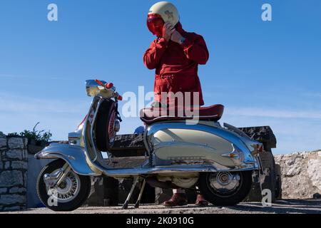 Homme en veste rouge sur le point de monter Lambretta TV 175 vintage scooter italien lors du rassemblement du rassemblement des Clans. Ballintoy, Royaume-Uni - 10 septembre 2022. Banque D'Images