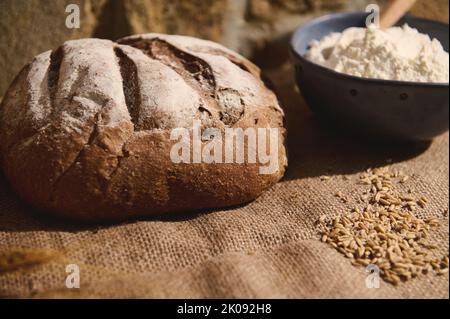 Encore la vie avec du pain de lactosérum de levain frais, des épis de blé et des ingrédients de cuisson sur une nappe en toile de jute Banque D'Images