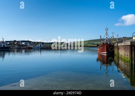 Dingle, Irlande - 7 août 2022 : bateau de pêche rouge sur les quais du port de Dingle dans le comté de Kerry avec des réflexions dans l'eau calme Banque D'Images