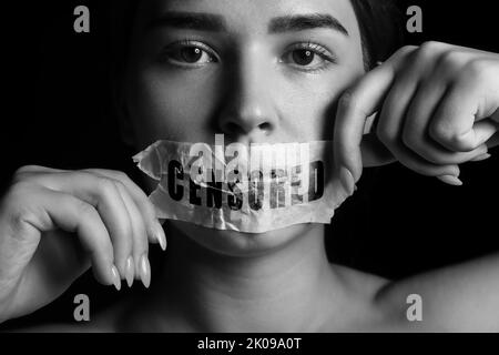 Portrait noir et blanc d'une femme avec une bouche collée sur un fond sombre. Concept de censure Banque D'Images