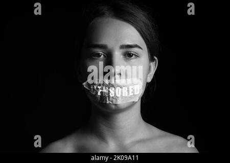 Portrait noir et blanc d'une femme avec une bouche collée sur un fond sombre. Concept de censure Banque D'Images