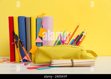 Étui à crayons avec papeterie scolaire et livres sur table sur fond jaune Banque D'Images