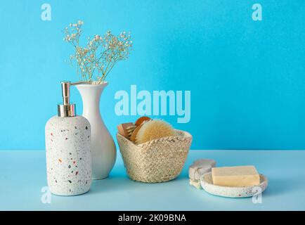 Accessoires de bain avec fleurs dans vase sur fond bleu Banque D'Images