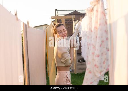 Jour de blanchisserie. Une femme porte du linge et des serviettes sur un arbre dans la cour d'une maison de village. Concept de chalet d'été. Banque D'Images