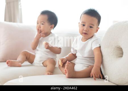 De jolis petits bébés chinois assis sur un canapé Banque D'Images