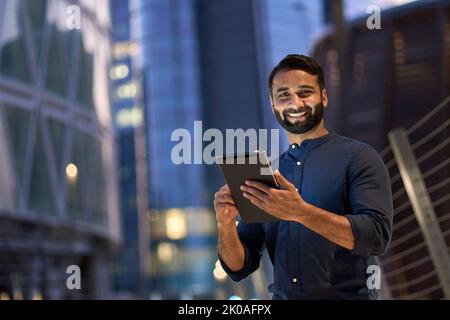 Homme d'affaires indien souriant tenant une tablette numérique dans une ville nocturne. Banque D'Images