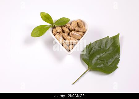 Pilules de fines herbes dans une plaque en forme de coeur et feuilles vertes sur fond bleu. Médecine alternative Banque D'Images