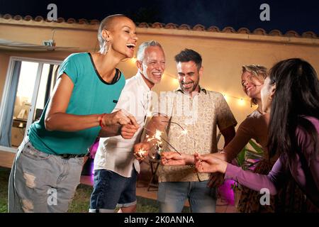 Un groupe d'amis matures fêtent avec étincelle à une fête privée dans l'arrière-cour ou dans un club. Des gens heureux et joyeux font la fête en plein air Banque D'Images