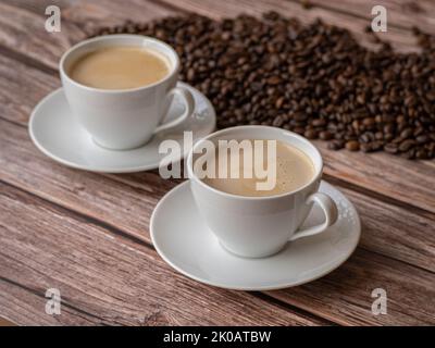 Deux tasses blanches avec café et lait sur table en bois. grains de café en arrière-plan Banque D'Images