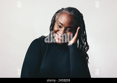 Une femme mûre et sûre d'elle-même souriant à la caméra tout en touchant ses dreadlocks. Une femme d'âge moyen et gaie embrassant ses cheveux naturels avec fierté. HAP Banque D'Images