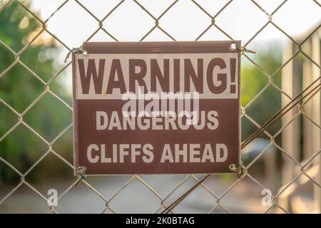 La Jolla, Californie - Avertissement dangereux Cliffs devant la signalisation. Gros plan d'une signalisation sur une clôture en treillis métallique sur un arrière-plan flou. Banque D'Images