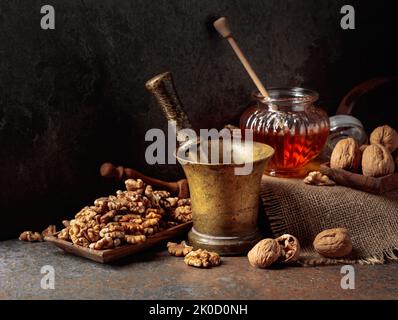 Noix, vieux mortier de laiton et miel sur une table de cuisine. Banque D'Images