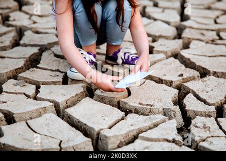 La fille abaisse le bateau en papier sur le sol sec et fissuré. Crise de l'eau et changement climatique concept. Réchauffement de la planète Banque D'Images