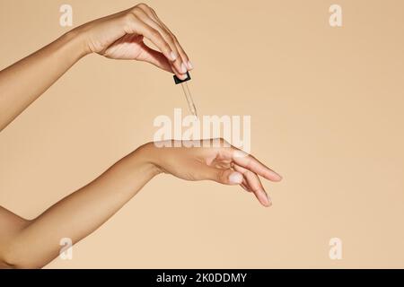 Hydrater la peau des mains avec de l'huile essentielle ou du sérum. Femme appliquant de l'huile essentielle sur ses mains avec pipette compte-gouttes sur fond beige Banque D'Images