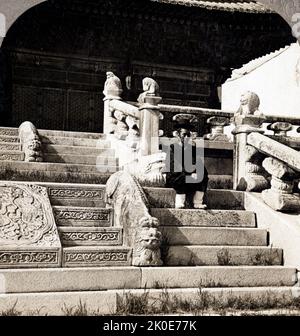 Joseon Era, Corée, 1890-1900. Un serviteur du Palais royal coréen assis sur les marches d'un bâtiment dans le Palais royal de Séoul. Banque D'Images