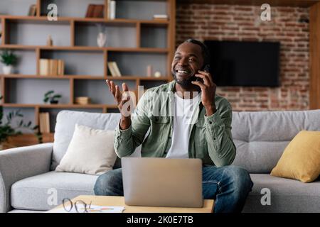 Entreprise et freelance à distance. Bon homme noir adulte dans une ambiance décontractée ont l'appel par smartphone, fonctionne avec un ordinateur portable Banque D'Images