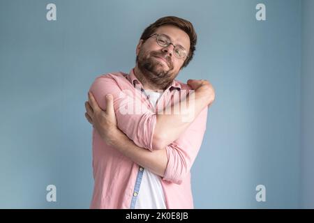 Rêvant de l'amour, un homme en lunettes et une chemise se déchègue doucement, debout sur un fond bleu. Banque D'Images
