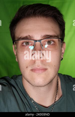 Gros plan de rendre le selfie attrayant beau et élégant homme en lunettes portant un t-shirt gris, atractive jeune homme visage gros plan sur fond vert chr Banque D'Images