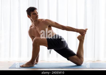 Jeune homme sportif qui s'étire les jambes sur un tapis de yoga pendant l'entraînement du matin Banque D'Images