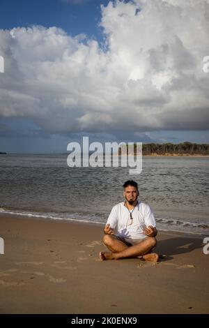 Jeune homme barbu assis faisant du yoga sur la plage. Détente dans la nature Banque D'Images