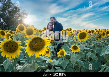 Homme en chemise bleue embrassant une femme dans une chemise blanche tout en se tenant au milieu d'un beau champ de tournesol Lawrence Kansas Banque D'Images