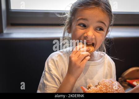 Une petite fille mange de la nourriture rapide dans un café. Banque D'Images