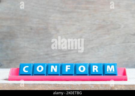 Lettre de l'alphabet de tuile avec le mot conforme dans le portoir de couleur rouge sur fond de bois Banque D'Images