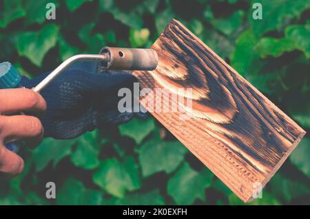 Un homme brûle des planches avec le feu d'un brûleur à gaz. Traitement du bois pour révéler la belle texture du bois. Banque D'Images