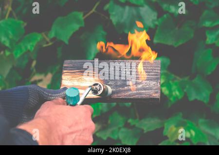 Un homme brûle des planches avec le feu d'un brûleur à gaz. Traitement du bois pour révéler la belle texture du bois. Banque D'Images