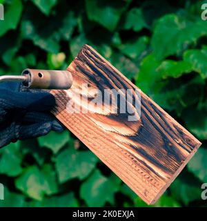 Un homme brûle des planches avec le feu d'un brûleur à gaz. Traitement du bois pour révéler la belle texture du bois. Banque D'Images