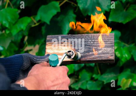 Un homme brûle des planches avec le feu d'un brûleur à gaz. Traitement du bois pour révéler la belle texture du bois. Banque D'Images