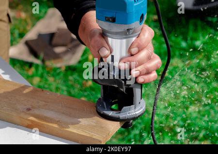 gros plan de menuisier avec machine à router à la main en bois au travail. gros plan de l'acheminement d'un biseau dans la planche de pin bois de construction concept d'outil fournit Banque D'Images