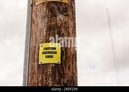 Panneau sur un poteau de téléphone en bois avertissant les gens que le poteau porte le câble de fibre optique. Banque D'Images