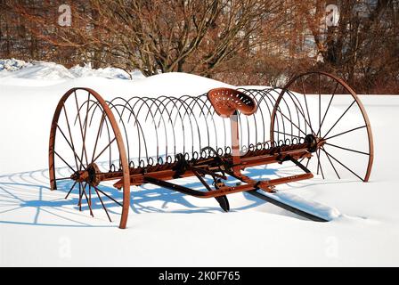 Une couche de métal d'époque et rouillé se trouve dans un champ enneigé lors d'une journée d'hiver sur une ferme près de la ville historique de Deerfield, Massachusetts Banque D'Images