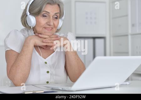 Femme âgée dans un casque suivre un cours en ligne sur ordinateur à la maison. Banque D'Images