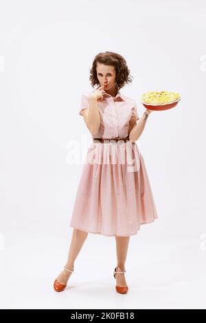 Portrait d'une belle femme émotive tenant la tarte aux pommes et la goûtant avec le doigt isolé sur fond blanc Banque D'Images