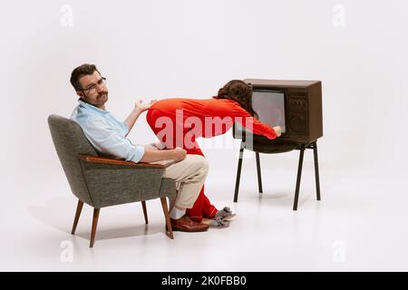 Portrait d'une femme de pyjama rouge qui éteint la télévision devant son mari. Besoin d'attention Banque D'Images