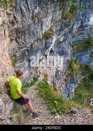 Garçon en chemise jaune rester au sommet de la voie avec chaîne en acier ancrée dans le mur rocailleux, chemin via le style ferrata. Nom du chemin en Italie Sentieri Attrezzato D. Banque D'Images