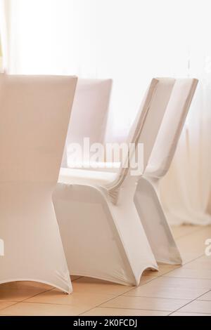 Chaises de banquet recouvertes de tissu blanc disposées dans la rangée pour préparer la réception de la cérémonie Banque D'Images