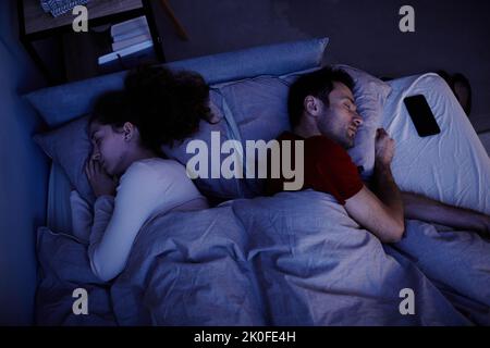 Vue en grand angle d'un jeune couple dormant sous une couverture dans le lit la nuit Banque D'Images