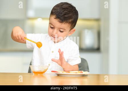 Petit garçon mignon et heureux mangeant de la pomme avec du miel, tenant le balancier de miel. L'enfant s'amuse, célébrez le nouvel an juif Rosh Hashanah. Banque D'Images